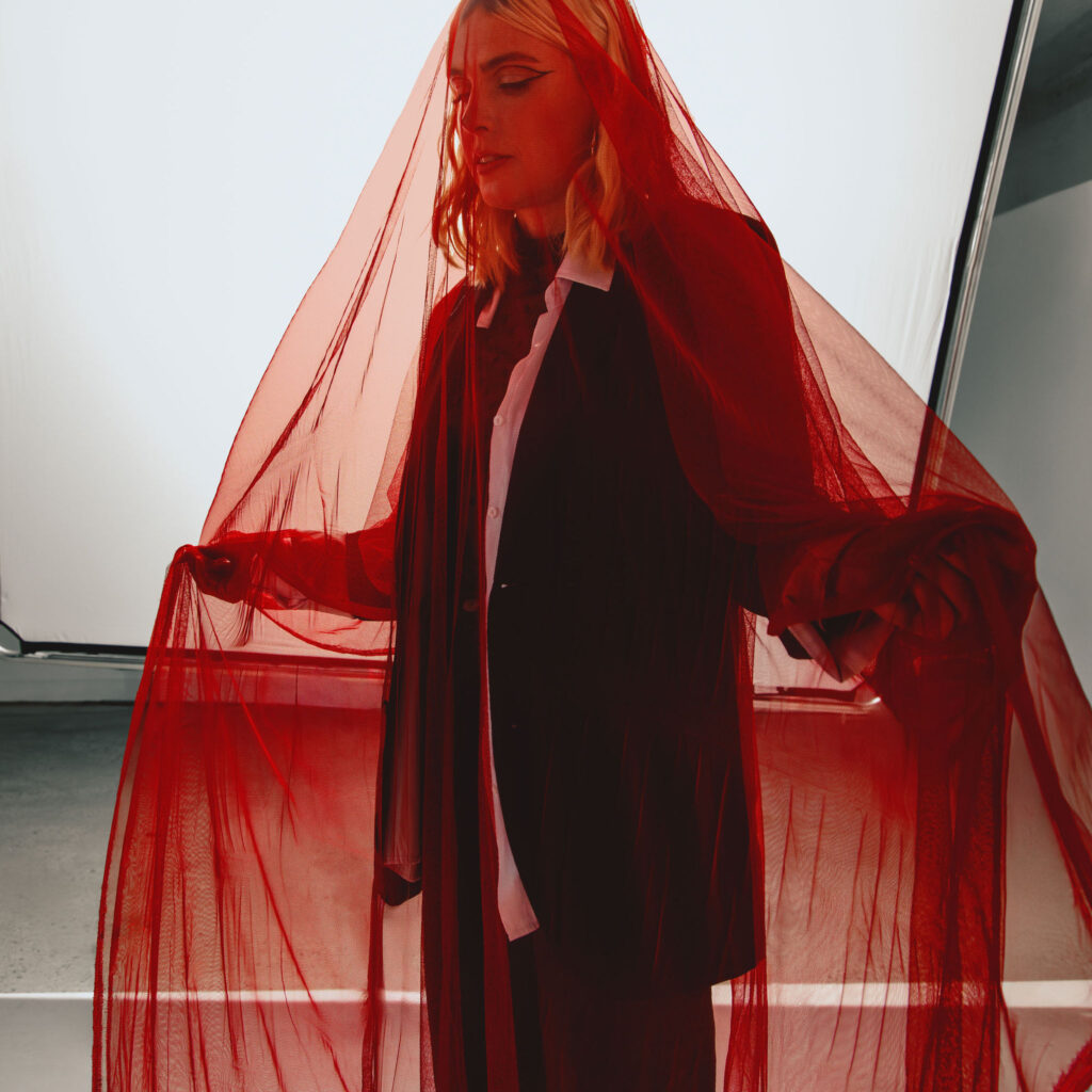 Q.E. in black suite with red sheer fabric over her.